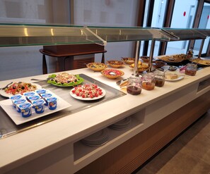 Un bufé con diversas opciones de comida y bebidas, como ensaladas, frutas y vasos de yogur.