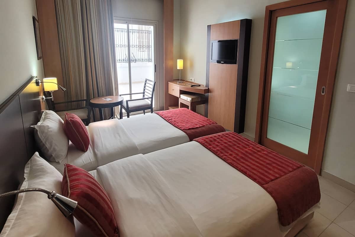 A hotel room with two beds, a desk, a chair, a TV, and a sliding door.