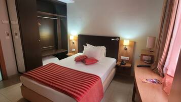 A hotel room with a large bed, a TV, a bedside table with a lamp, and a wooden nightstand.