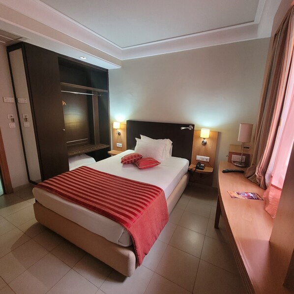 Habitación de hotel con una cama grande, televisión, mesita de noche con lámpara y un aparador de madera.