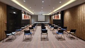 Ein Konferenzraum mit langem Tisch und Stühlen, einer Projektionsleinwand und einer Holzwand mit Kunstwerken.