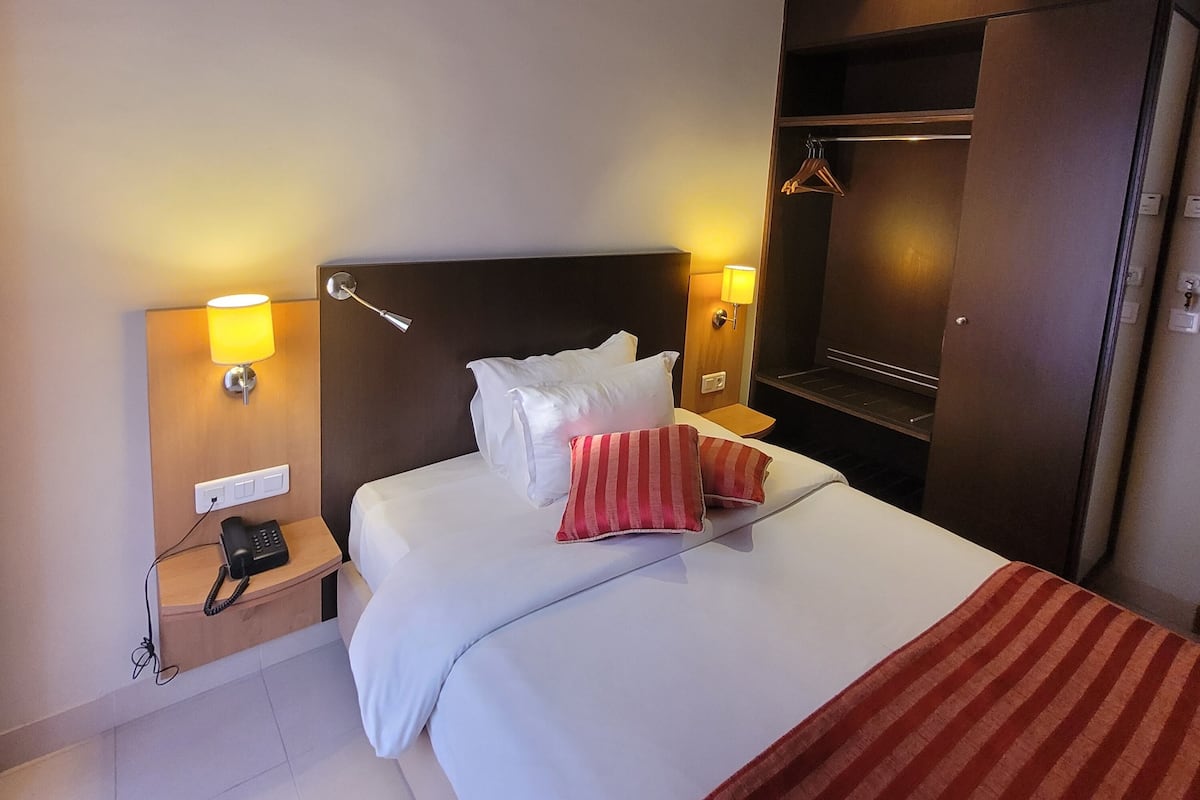 A hotel room with a bed, bedside lamps, a telephone, and a wardrobe.
