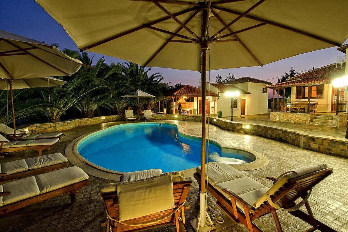 Una piscina con sillones de descanso y sombrillas, rodeada de muros de piedra y palmeras.