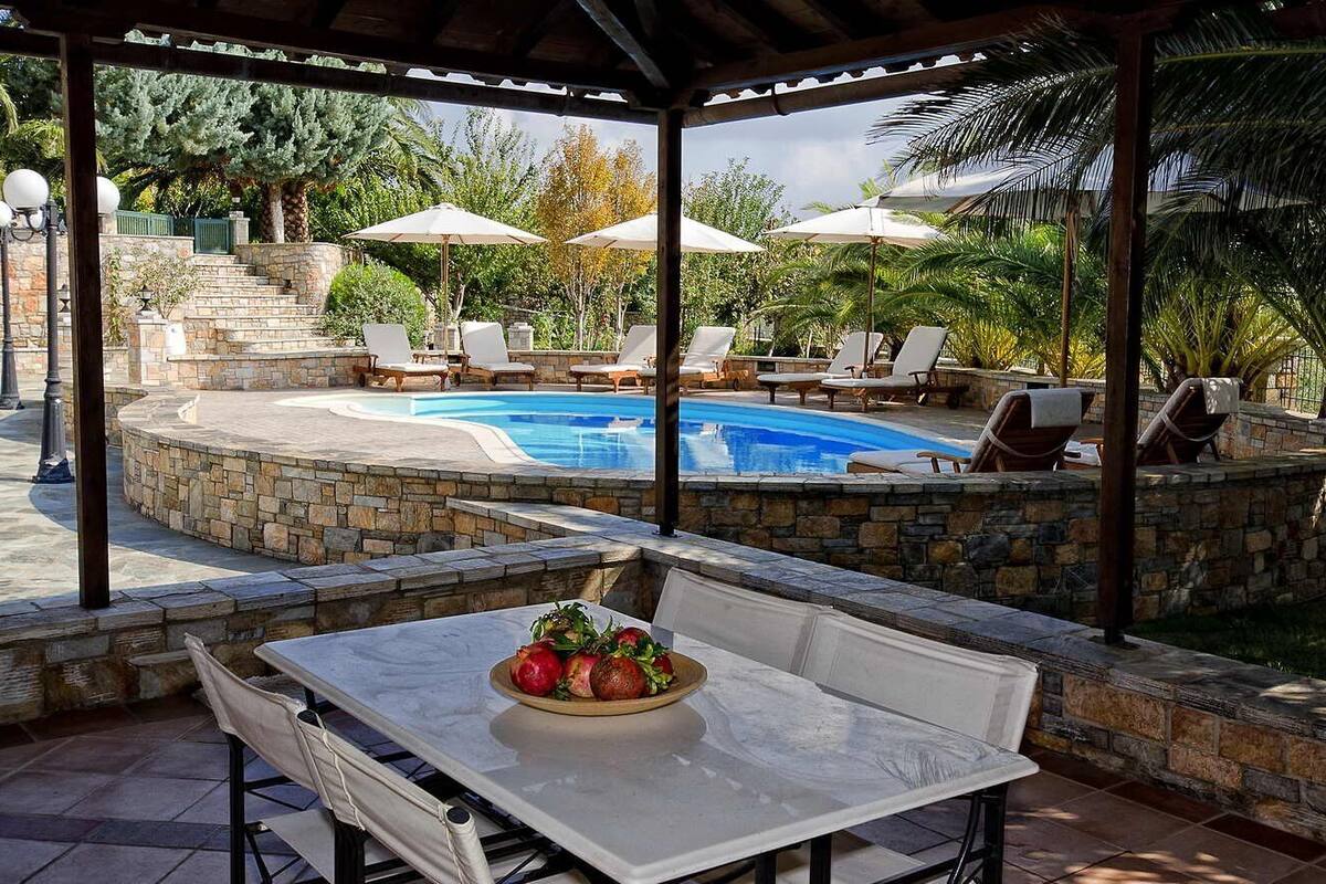 Un espacio al aire libre techado con piscina, sillas de descanso y una mesa con fruta.