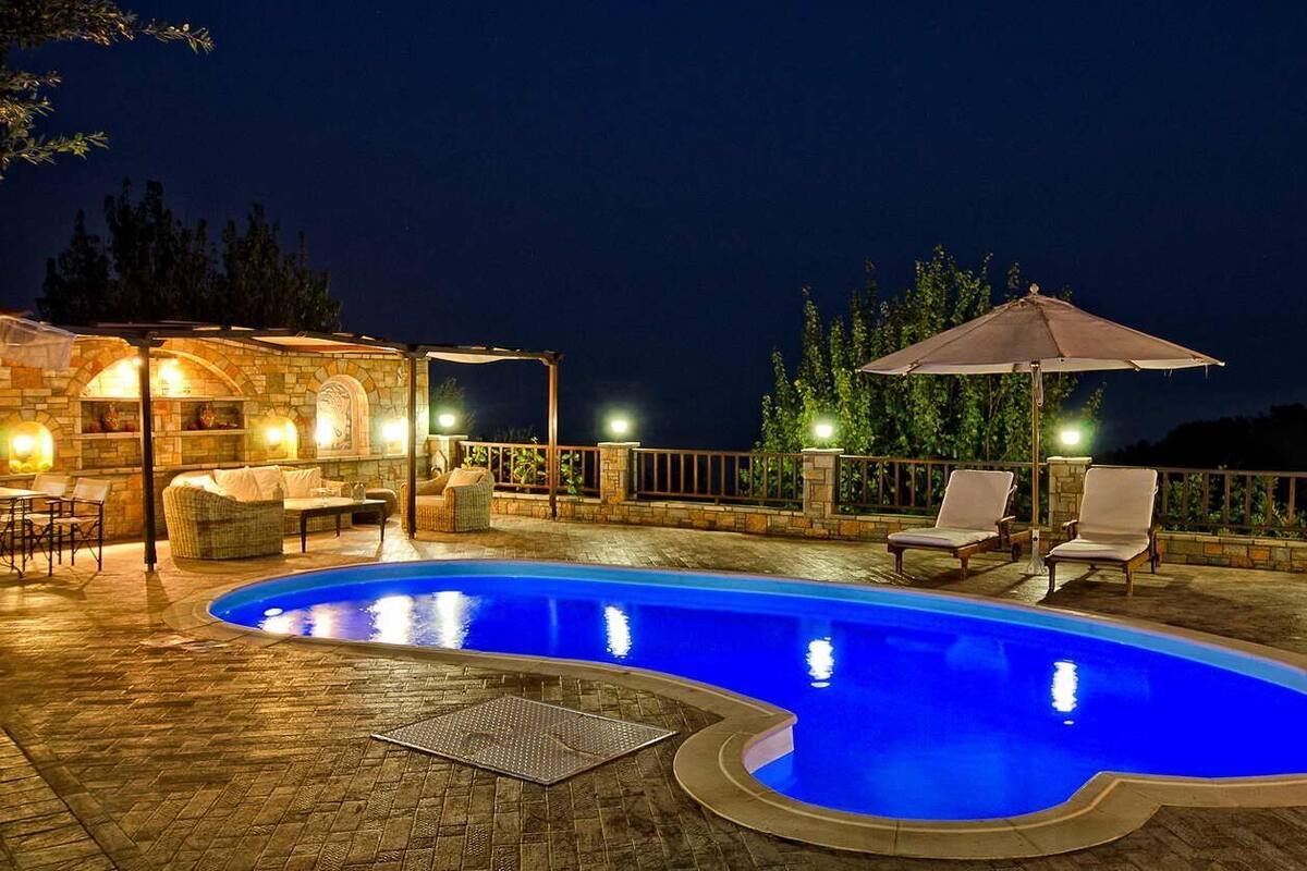 Una piscina al aire libre con cubierta de piedra, sillas de descanso y sombrillas.