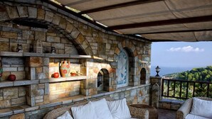 Una chimenea de piedra con estantes, una zona de estar con cojines y vistas al paisaje.
