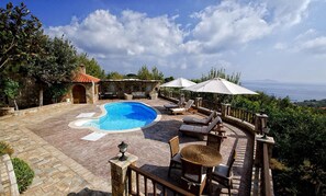 A pool area with lounge chairs and umbrellas, surrounded by stone walls and vegetation. - Vatellis Villas (Alonissos)