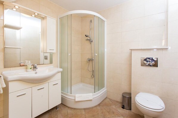A modern bathroom with a glass-enclosed shower, a white sink with a mirror, and a toilet. - Orka Apartments (Dubrovnik)