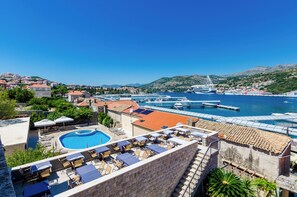 A rooftop pool with lounge chairs and umbrellas, a clear blue sky, and a marina with boats. - Orka Apartments (Dubrovnik)
