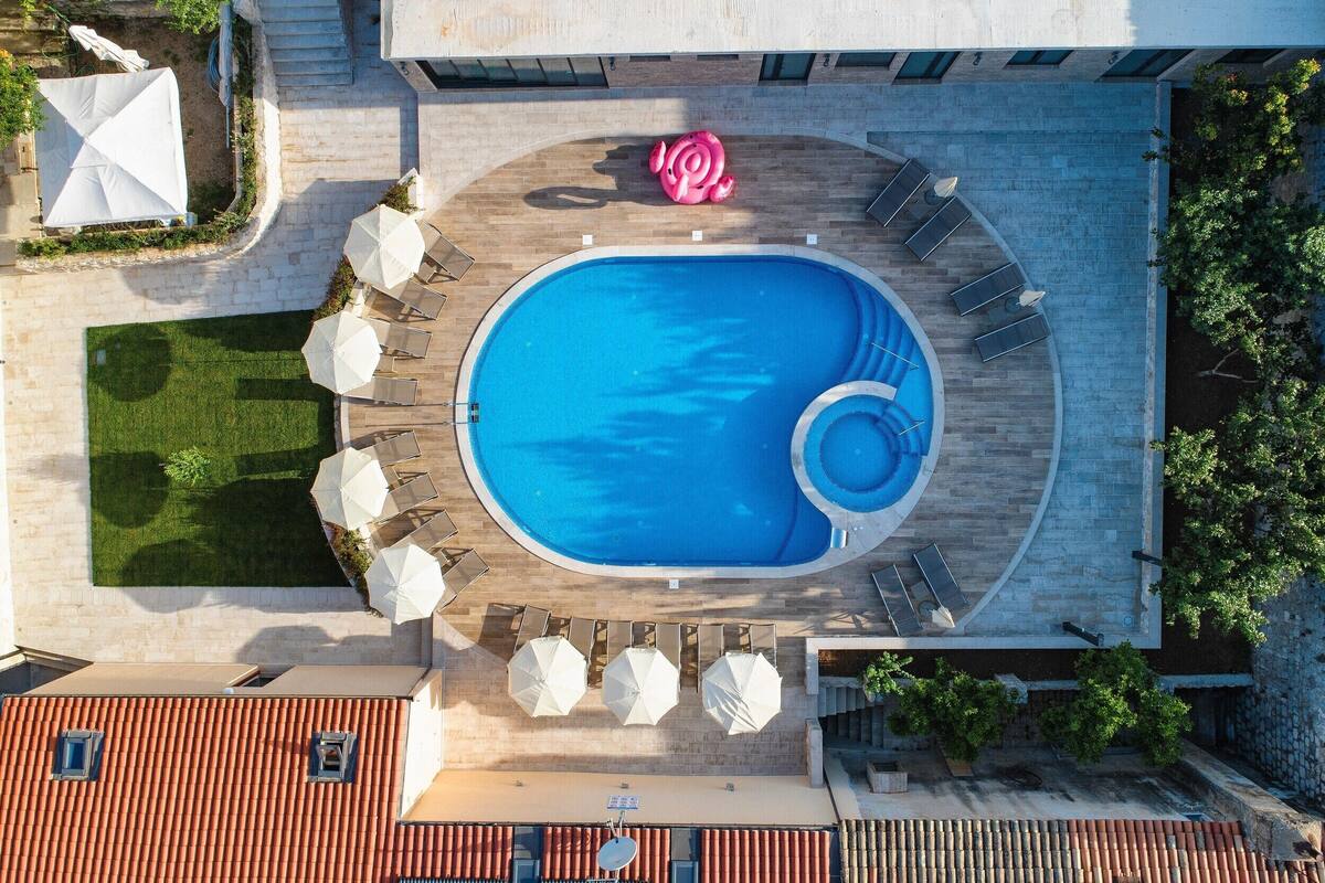 An aerial view of a rooftop swimming pool with a circular design, surrounded by lounge chairs and umbrellas.