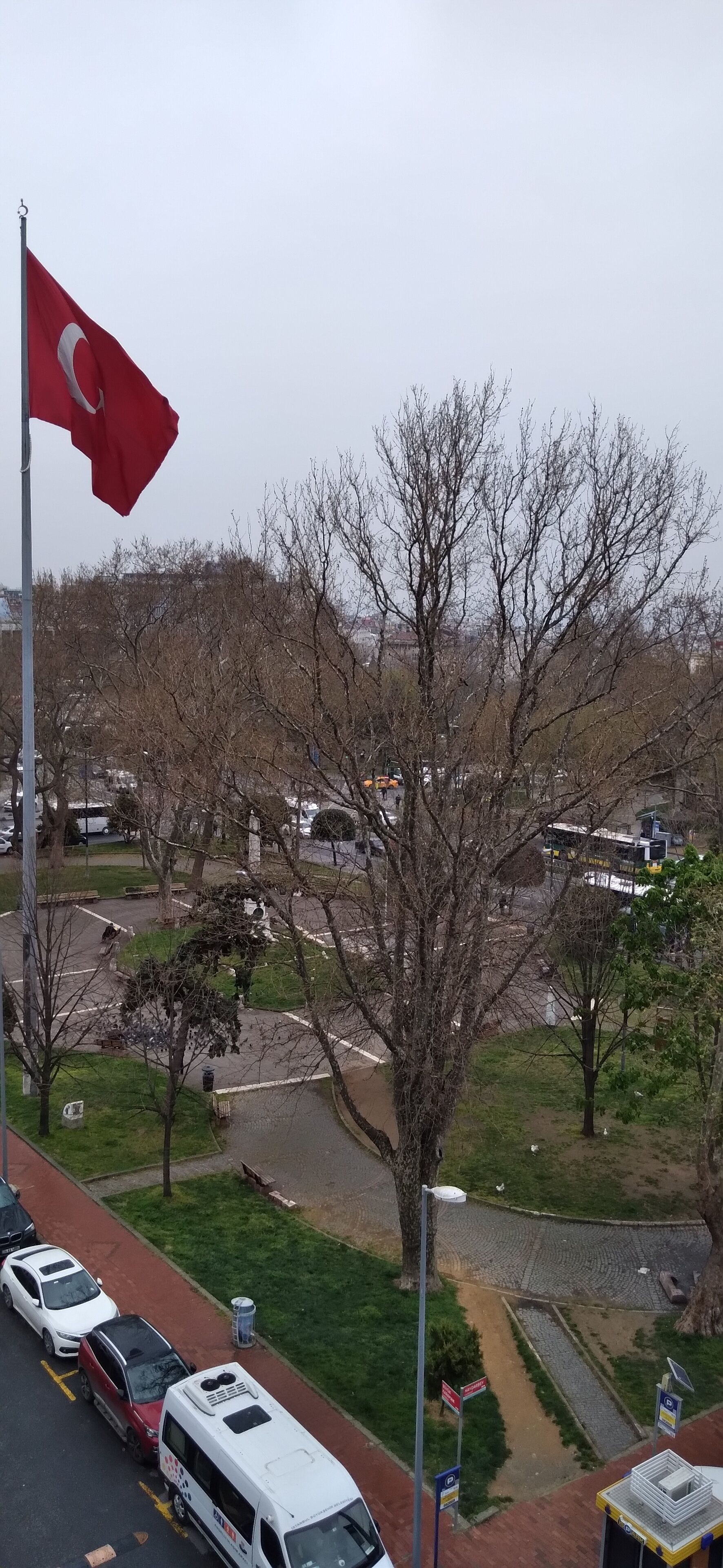 Un estacionamiento con una bandera roja, una camioneta blanca y un autobús.