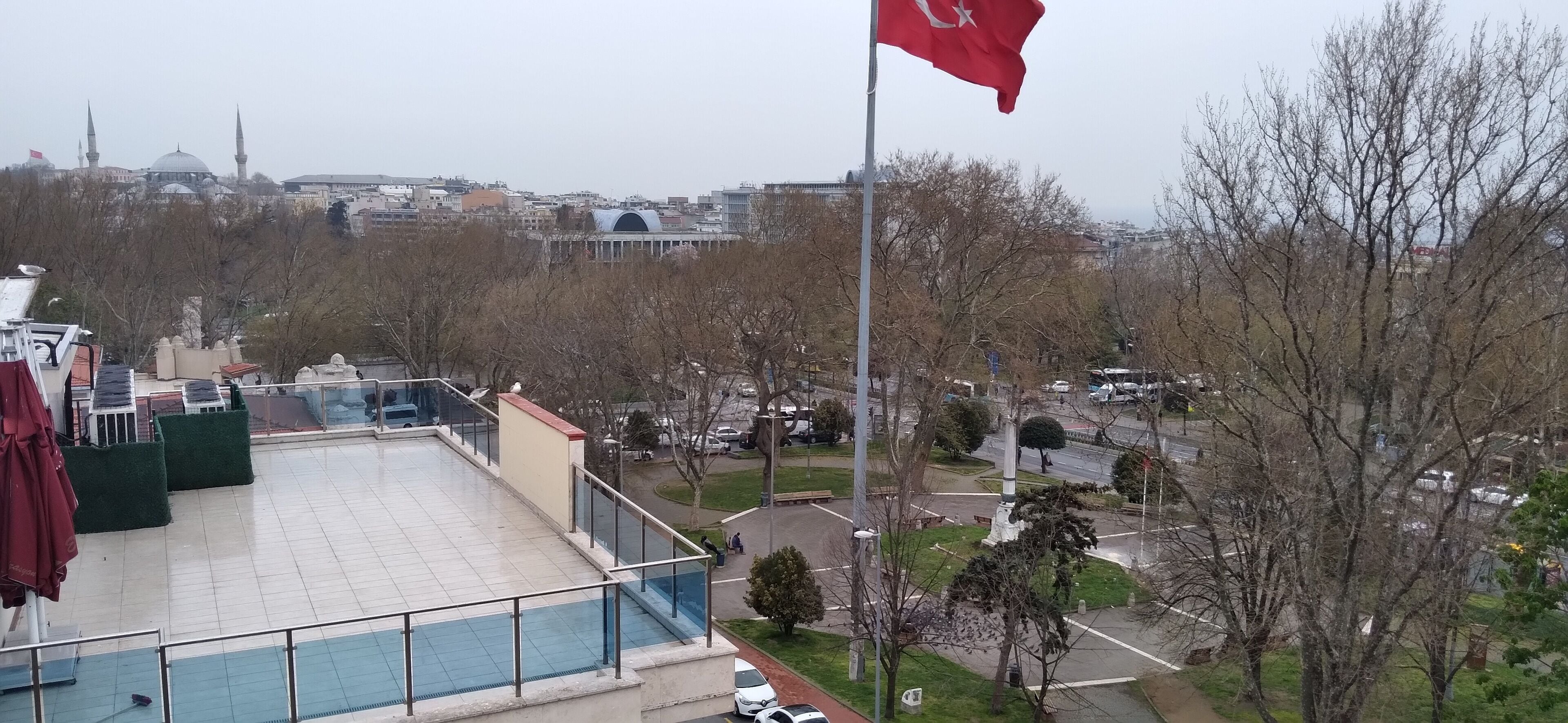 Une terrasse sur le toit, ornée d’un drapeau, avec une piscine et une vue sur le paysage urbain, qui comprend notamment une mosquée.