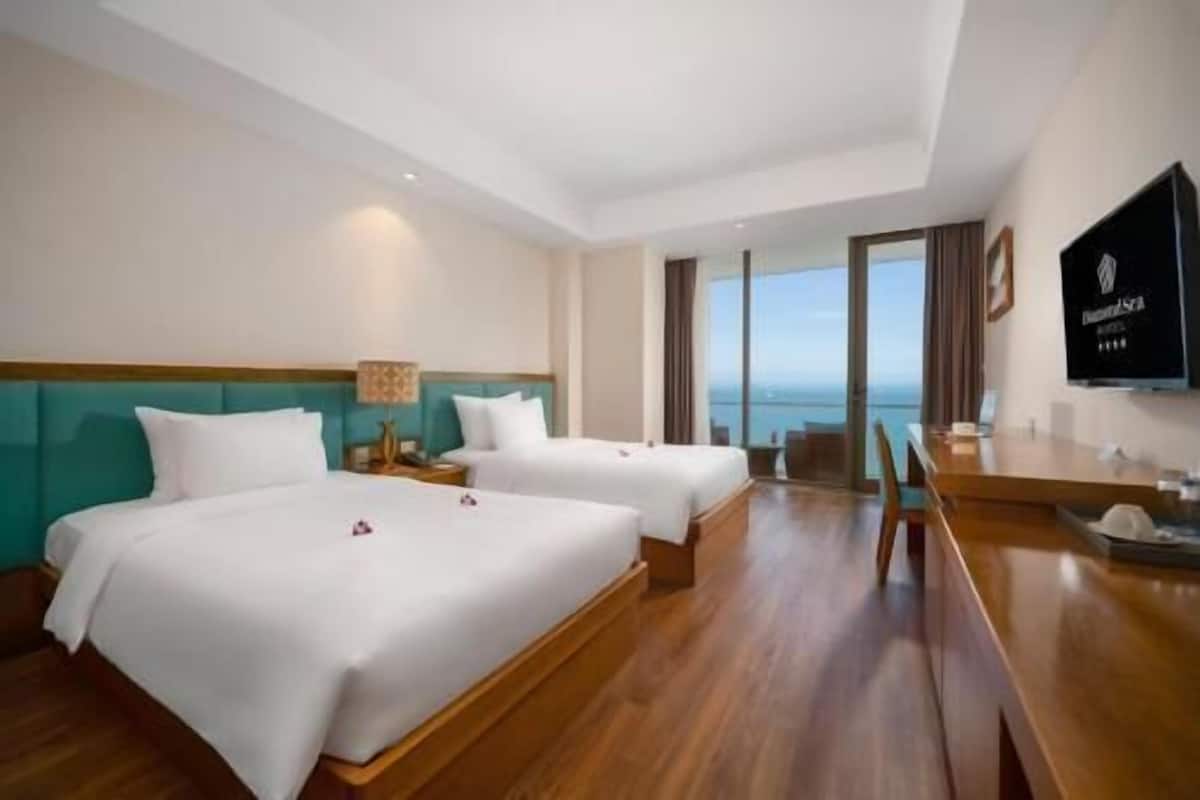 Habitación de hotel con dos camas, suelo de madera, televisor y vista al mar.
