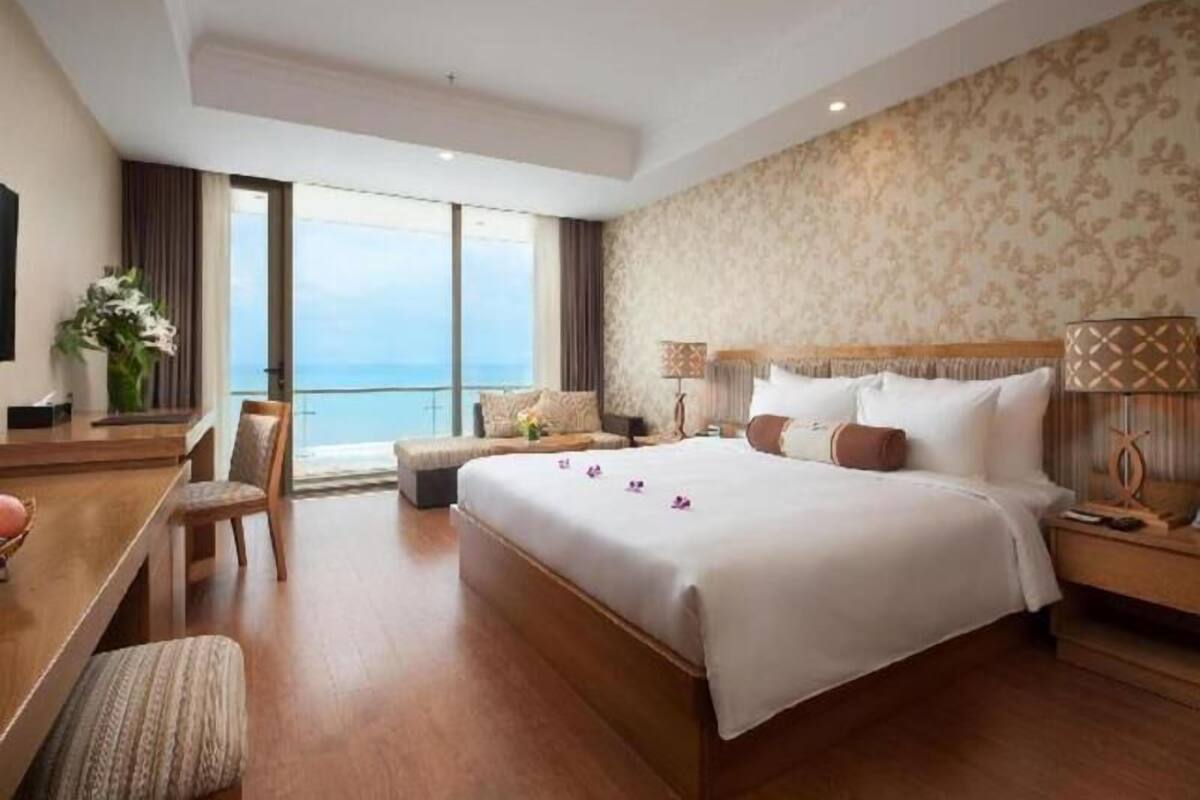 Una habitación de hotel con una cama grande, un escritorio con silla, una mesita, una lámpara y vistas al mar.