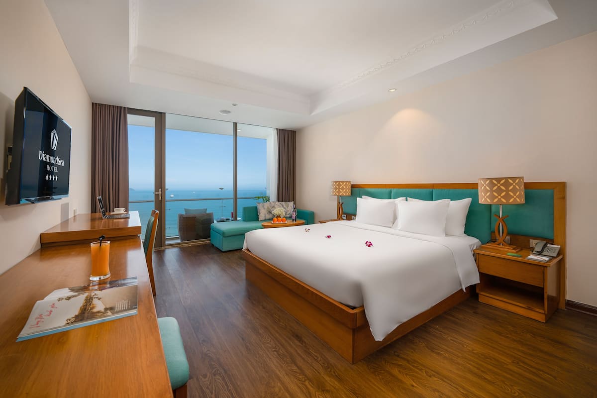 Habitación de hotel con una cama grande, un escritorio con televisión de pantalla plana, un sofá y vista al océano.