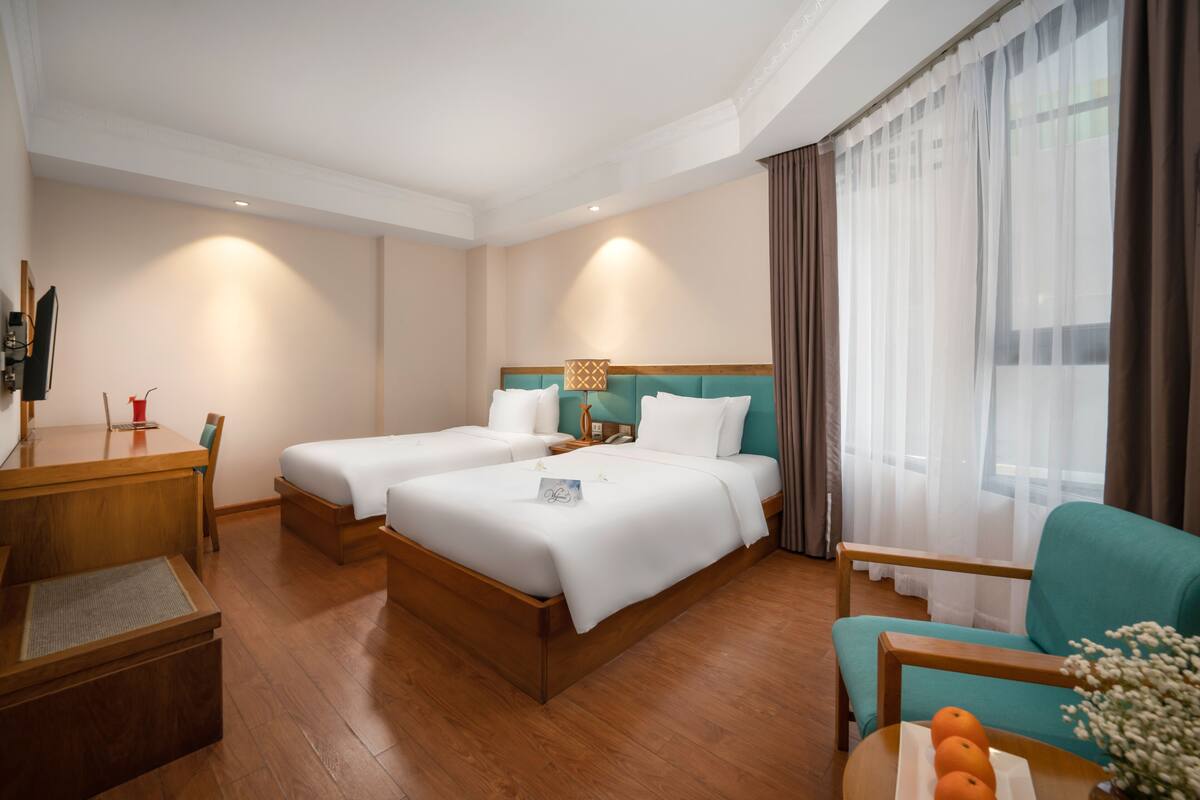 Una habitación de hotel con dos camas, un escritorio, una silla y una pequeña mesa con fruta.