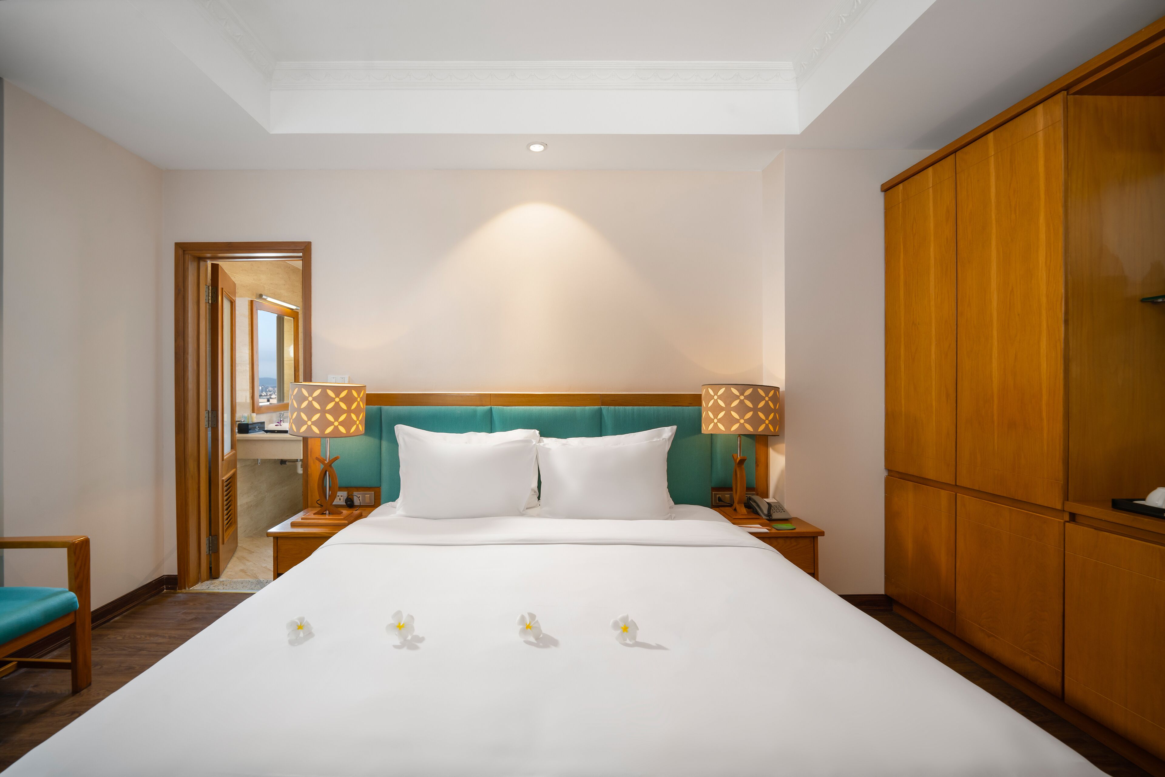 A hotel room with a large bed, two bedside tables, a wooden wardrobe, and a view of the city through a window.