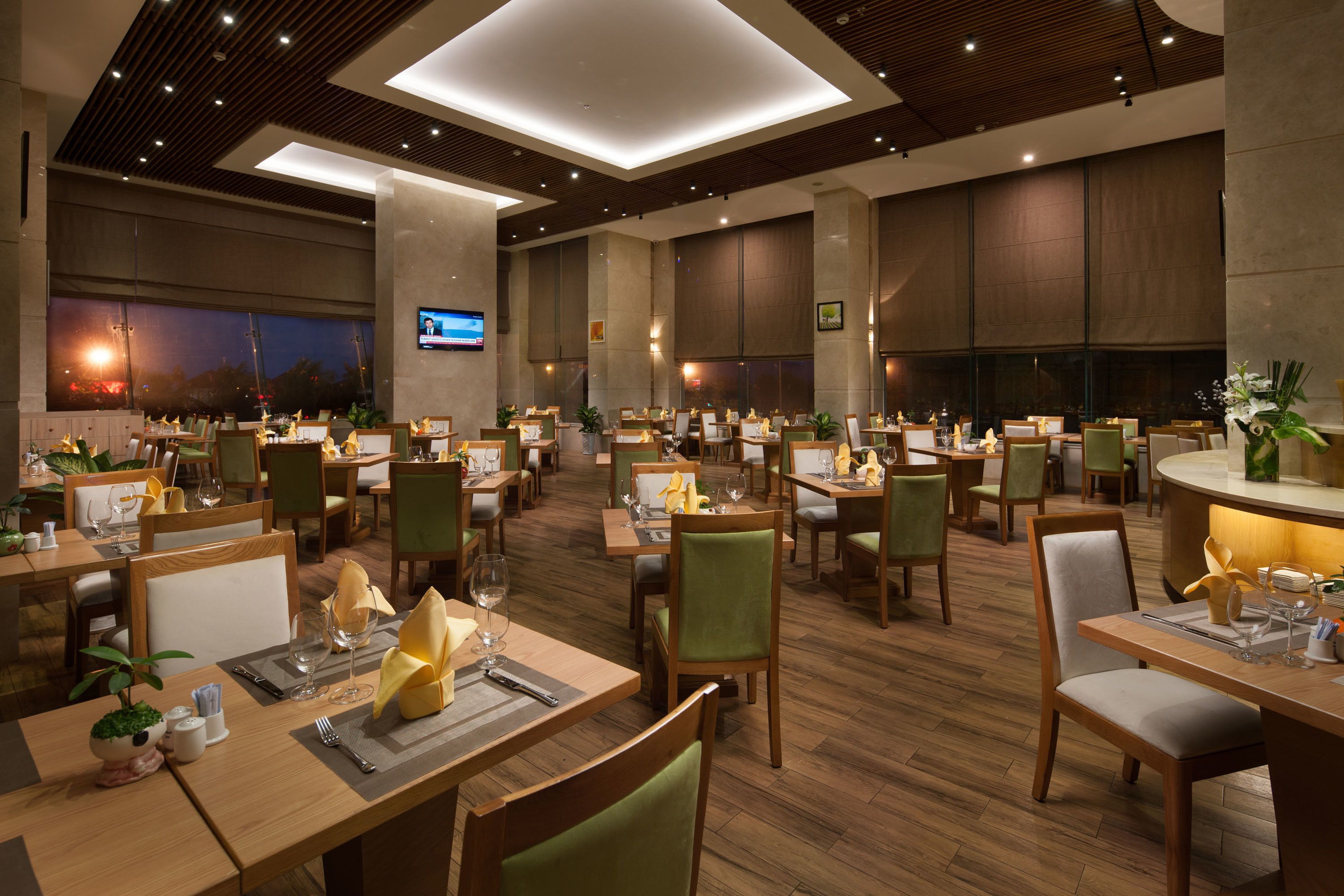 A spacious restaurant with multiple dining tables, chairs, and a television mounted on the wall.