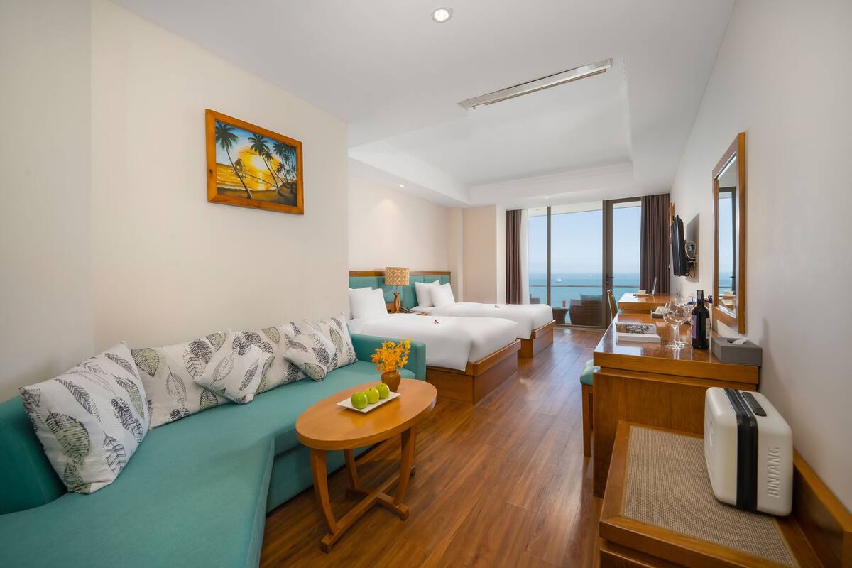 Habitación de hotel con sofá, dos camas, zona de comedor y vistas al océano.