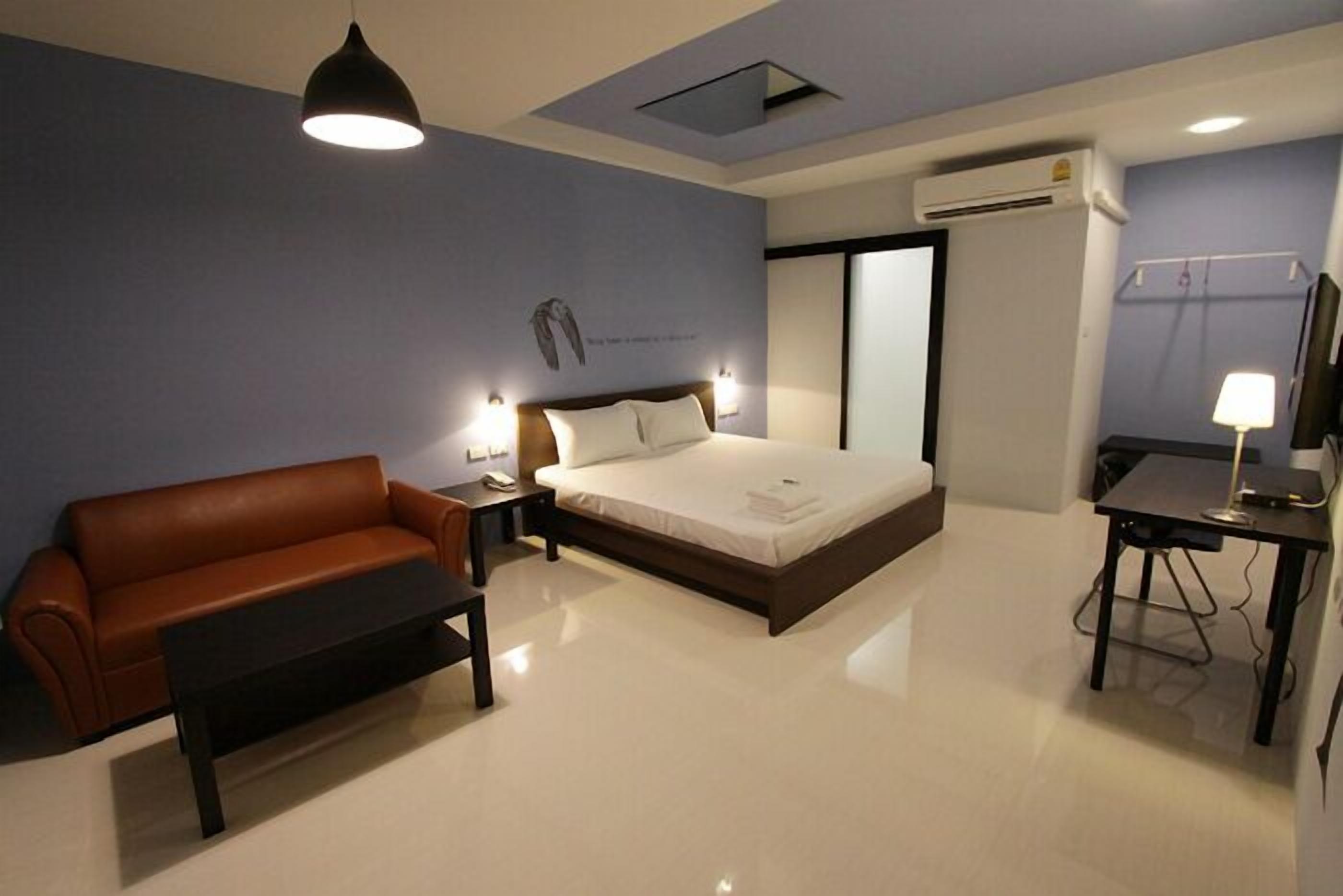 A hotel room with a bed, a sofa, a desk, and a lamp.