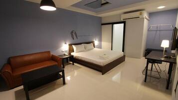 A hotel room with a bed, a sofa, a desk, and a lamp.