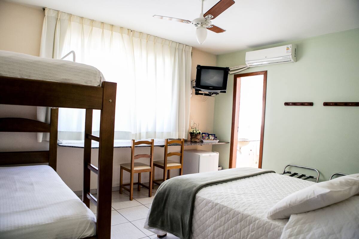 Een kamer met stapelbedden, een bureau met stoel, een televisie en een airconditioning.