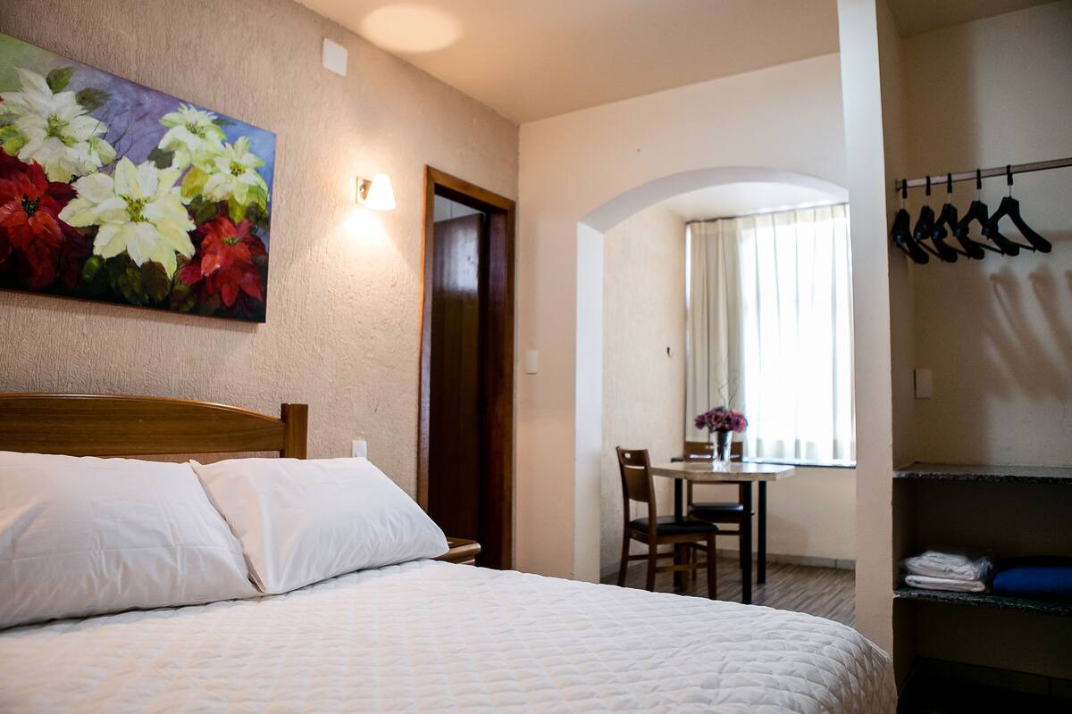 Een hotelkamer met een bed, een bloemschilderij, een zithoek en een kapstok.