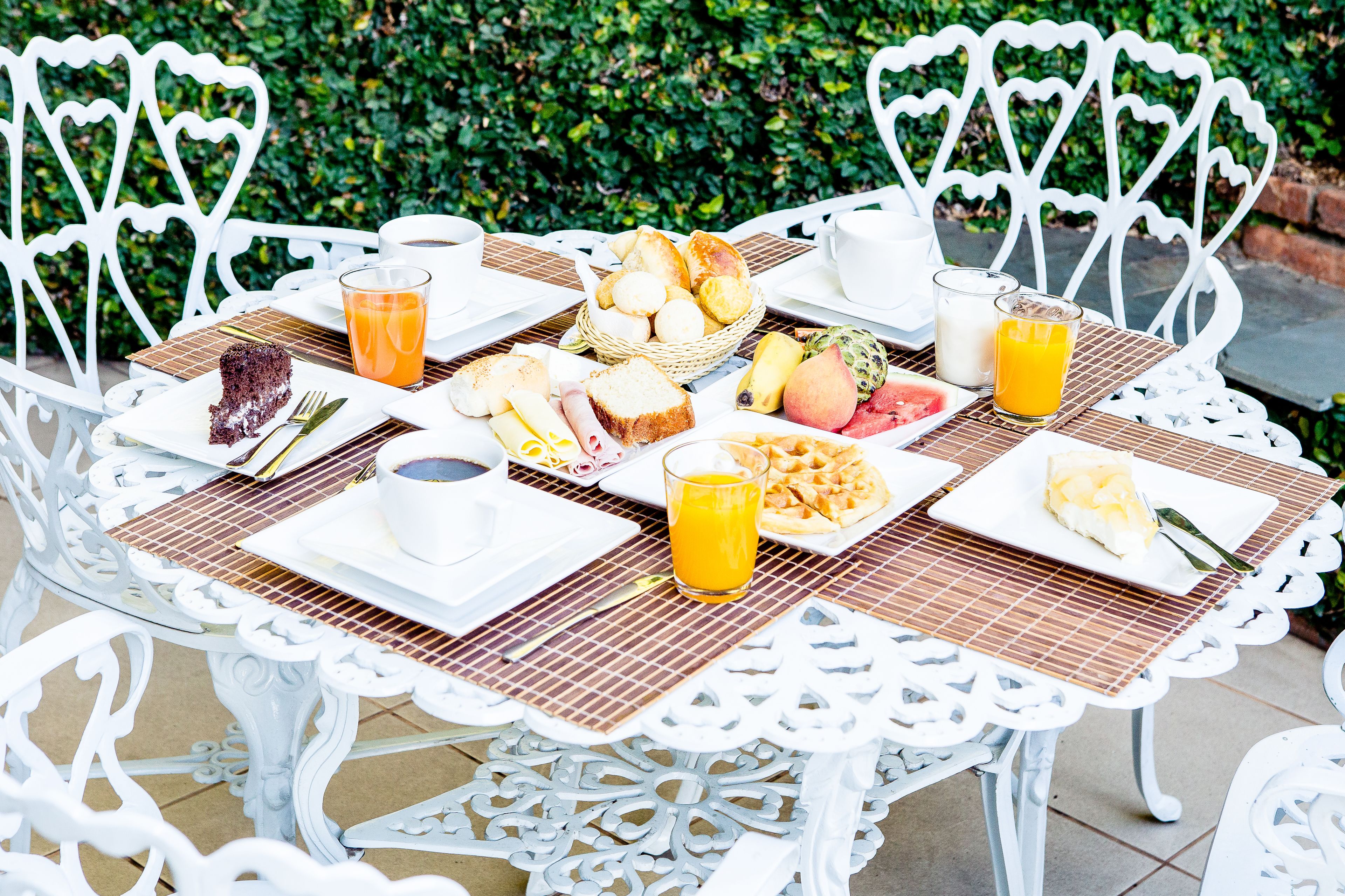 Een ontbijttafel met brood, fruit en een stukje taart, omringd door witte stoelen.