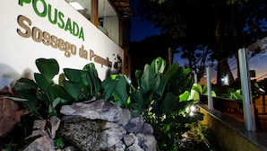 Une enseigne indiquant « Pousada Sossego da Pampulha », avec un mur en pierre et de grandes plantes vertes devant.