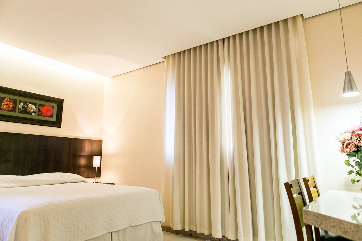 Een hotelkamer met een bed, een eettafel en een groot raam met gordijnen.