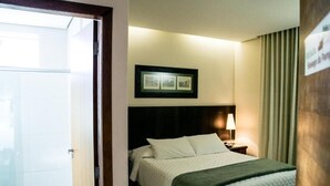 Une chambre d’hôtel avec un lit, une table de chevet avec une lampe, un tableau encadré au mur et une pancarte sur la porte.