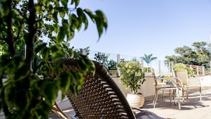Un espace patio aménagé avec des chaises et une table en osier, entouré de plantes en pot et offrant une vue dégagée sur le ciel.