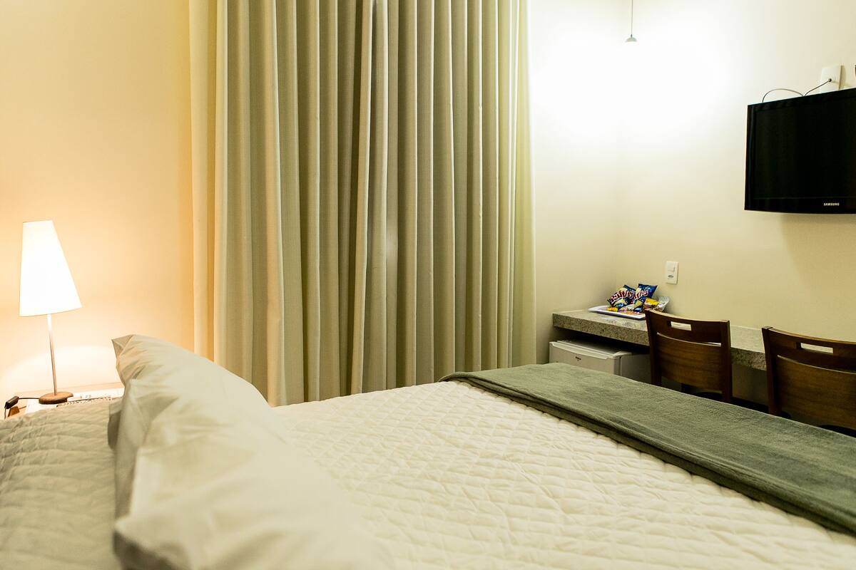 Een hotelkamer met een bed, een bureau met een lamp, een televisie en een raam met gordijnen.