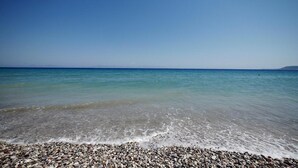 A pebbly beach with clear turquoise water and a distant mountain range.