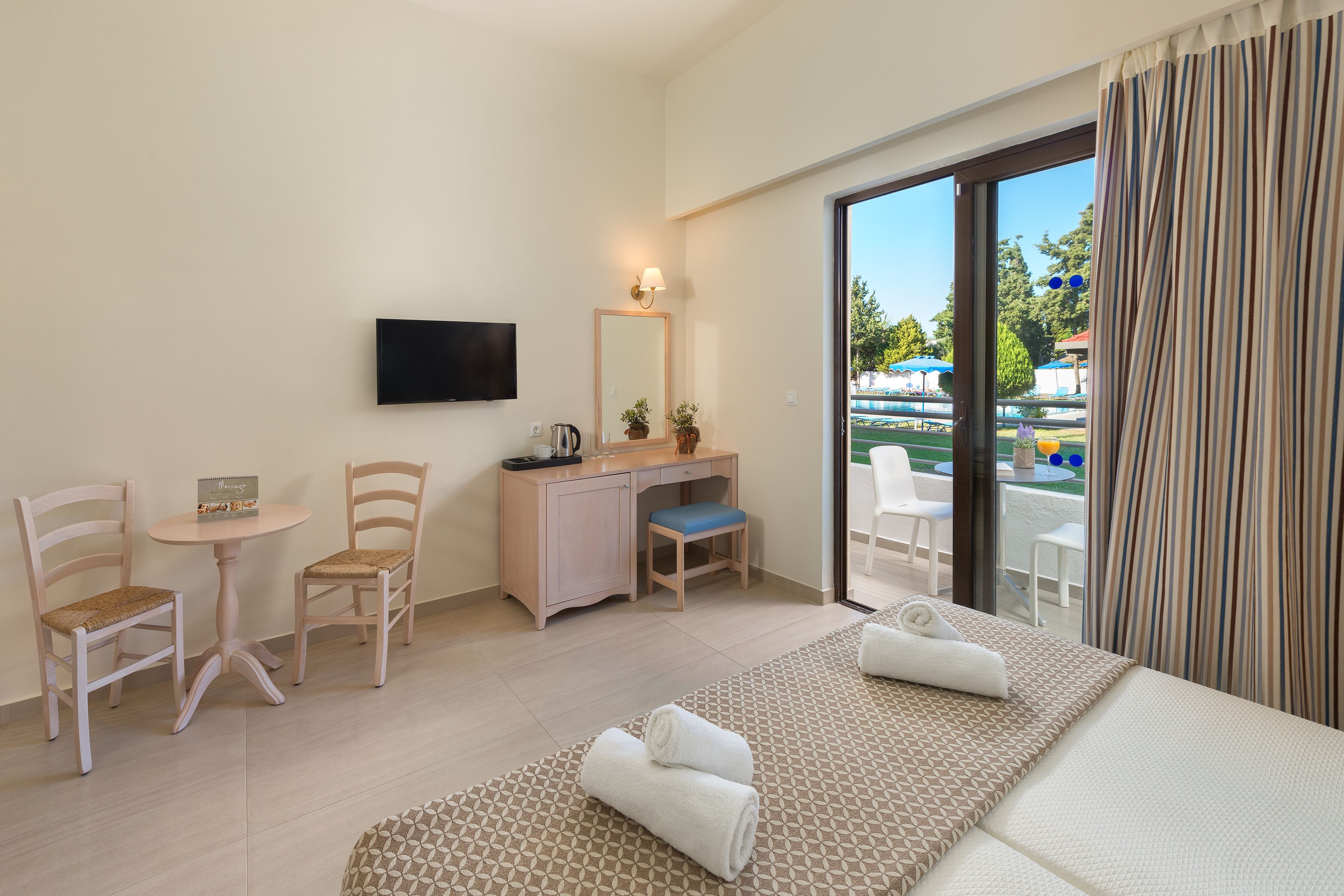 Quarto de hotel com cama, duas cadeiras, escrivaninha, televisão e vista para o exterior.