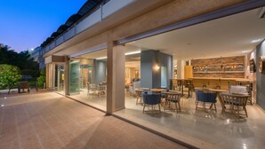 An outdoor seating area with tables and chairs, a glass door entrance, and a brick wall interior.