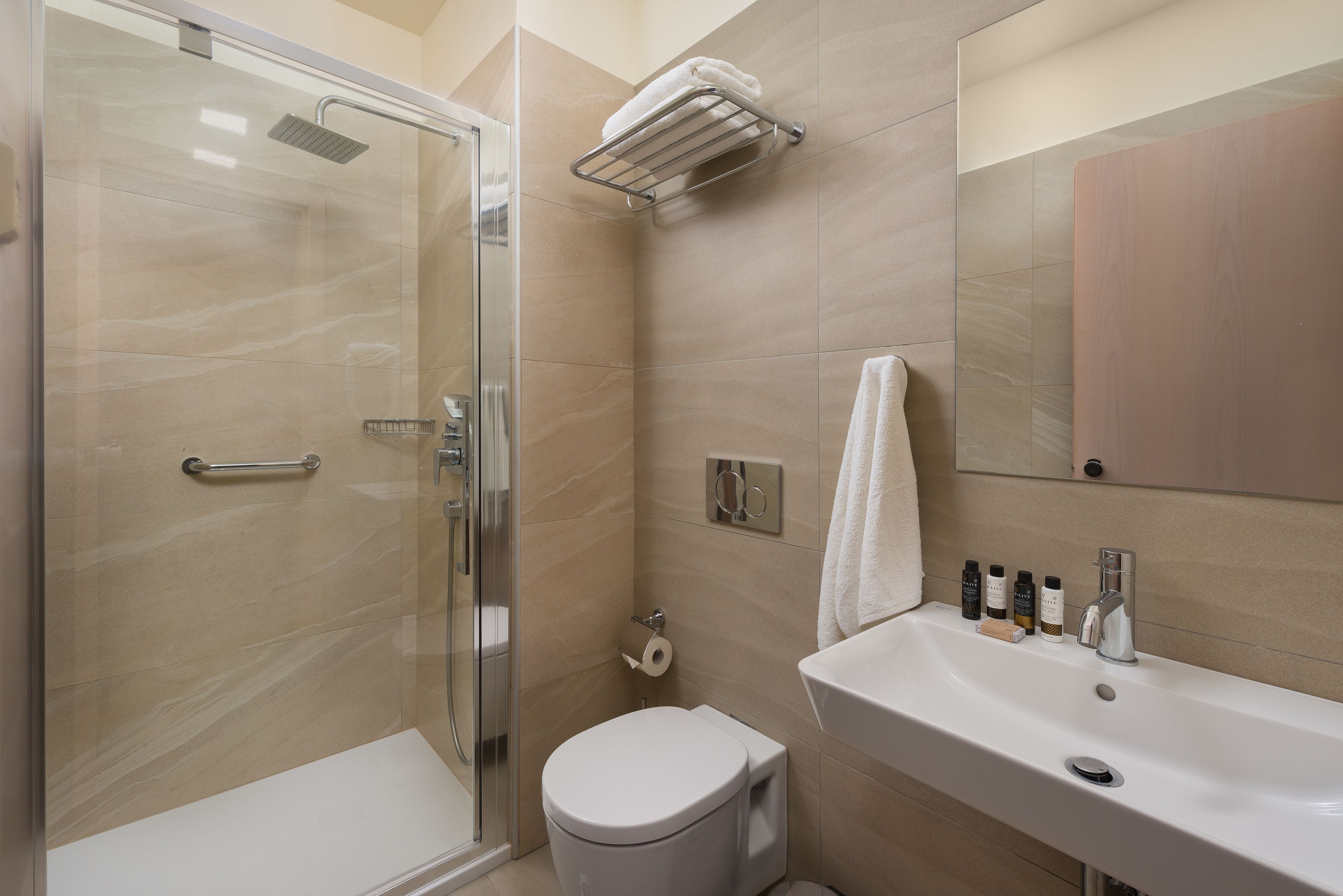 A bathroom with a glass shower enclosure, a toilet, a sink with toiletries, and a towel rack.