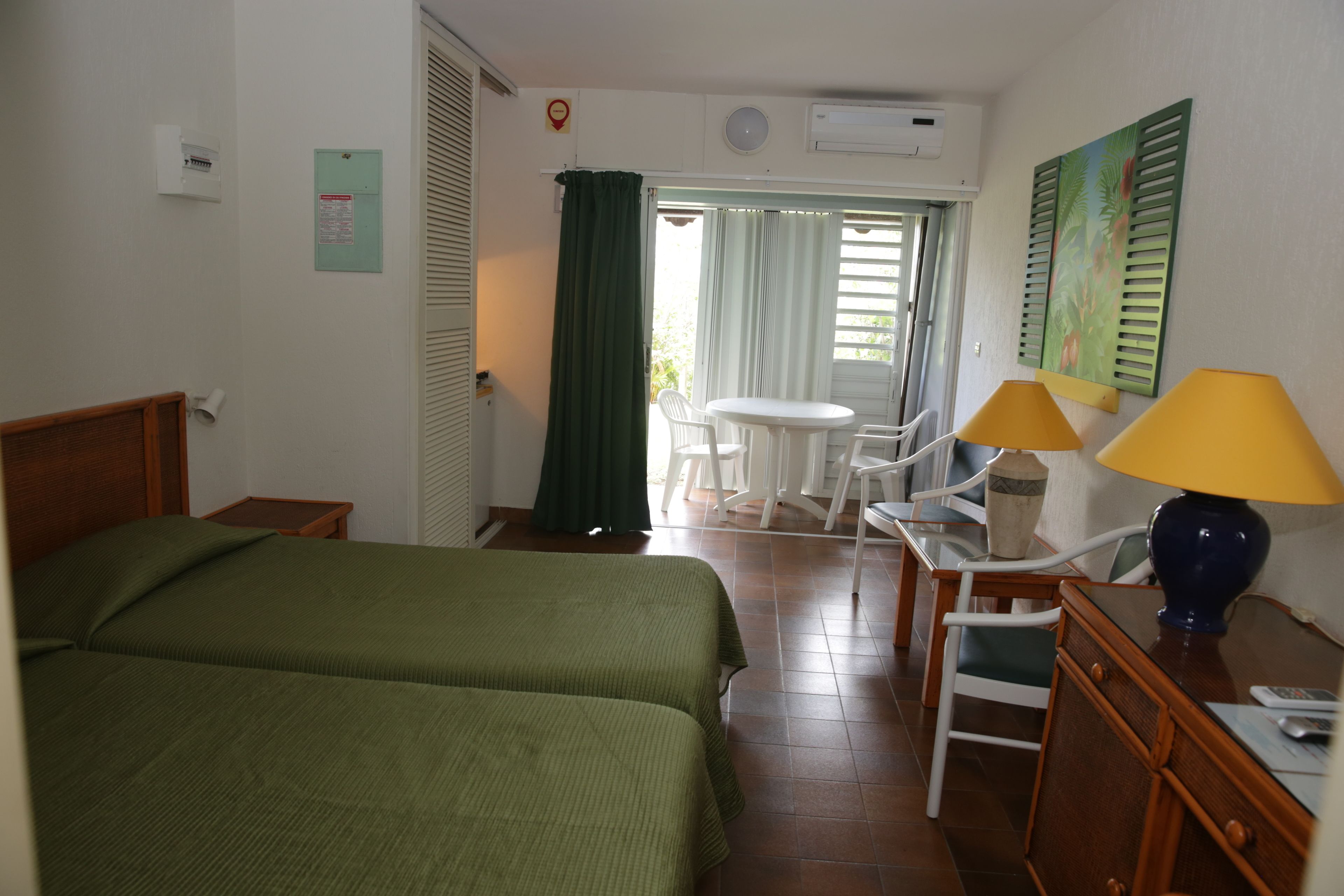 Ett hotellrum med två sängar, ett skrivbord med en lampa, en stol, ett litet bord och ett fönster med gardiner.