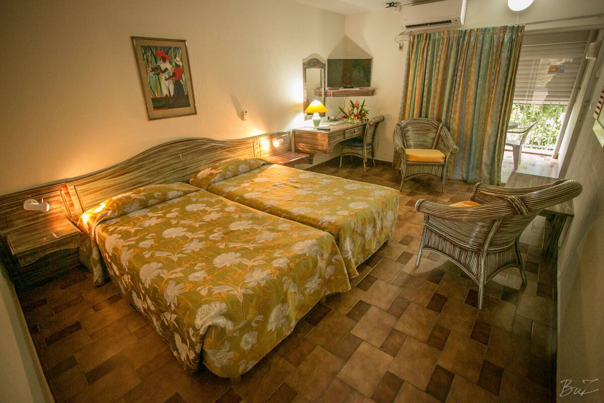 A hotel room with two beds, a desk, a chair, and a balcony with curtains.