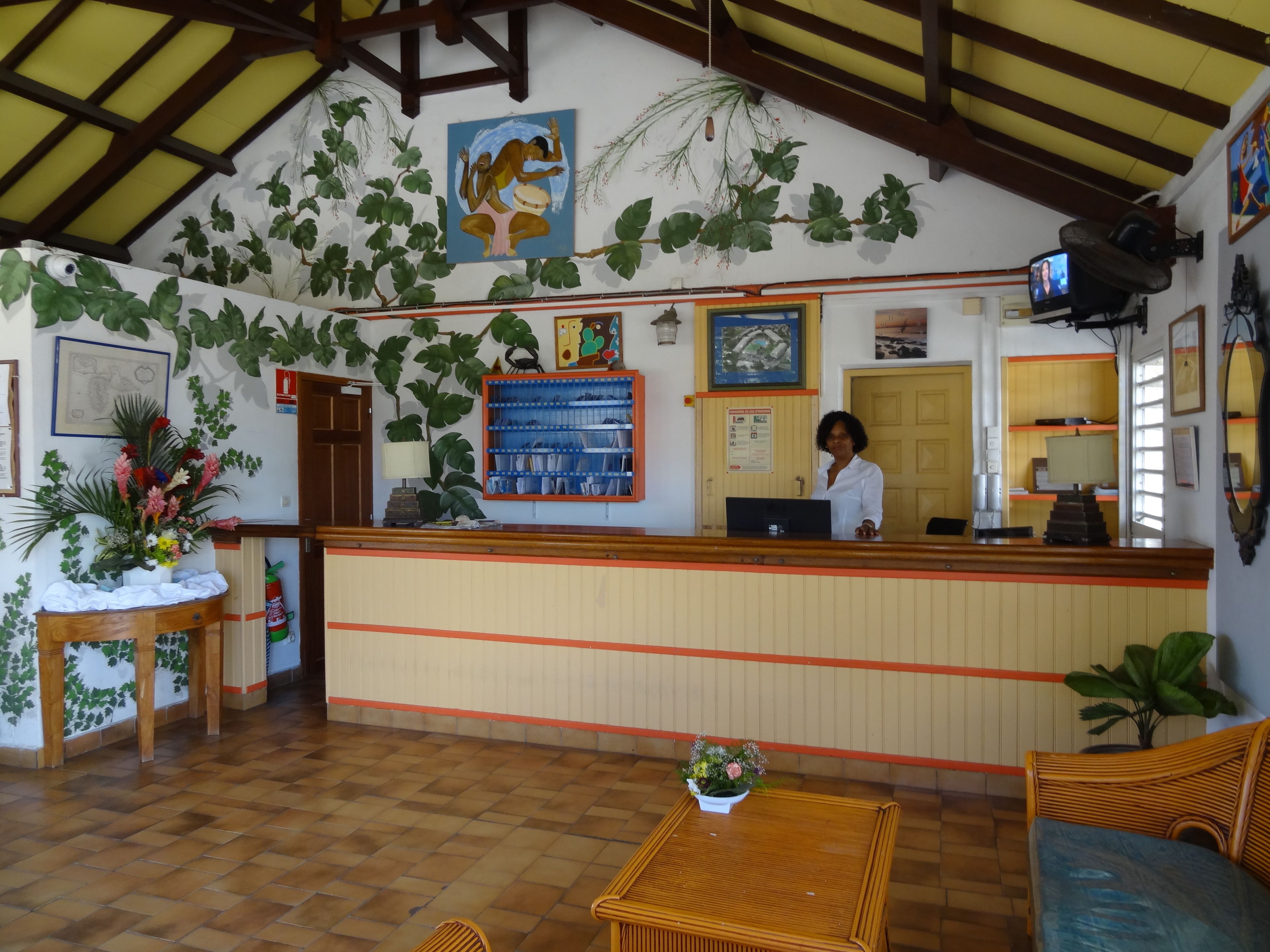 A reception area with a wooden reception desk, a receptionist, a computer, a wall-mounted TV, and a large painting.