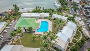 An aerial view of a resort with a swimming pool, multiple buildings, and a marina with boats. - Hotel Village Soleil (Le Gosier)