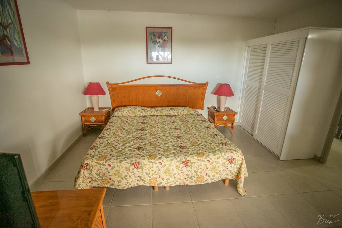 A bedroom with a floral bedspread, two bedside tables with lamps, a wardrobe, and a framed picture on the wall.