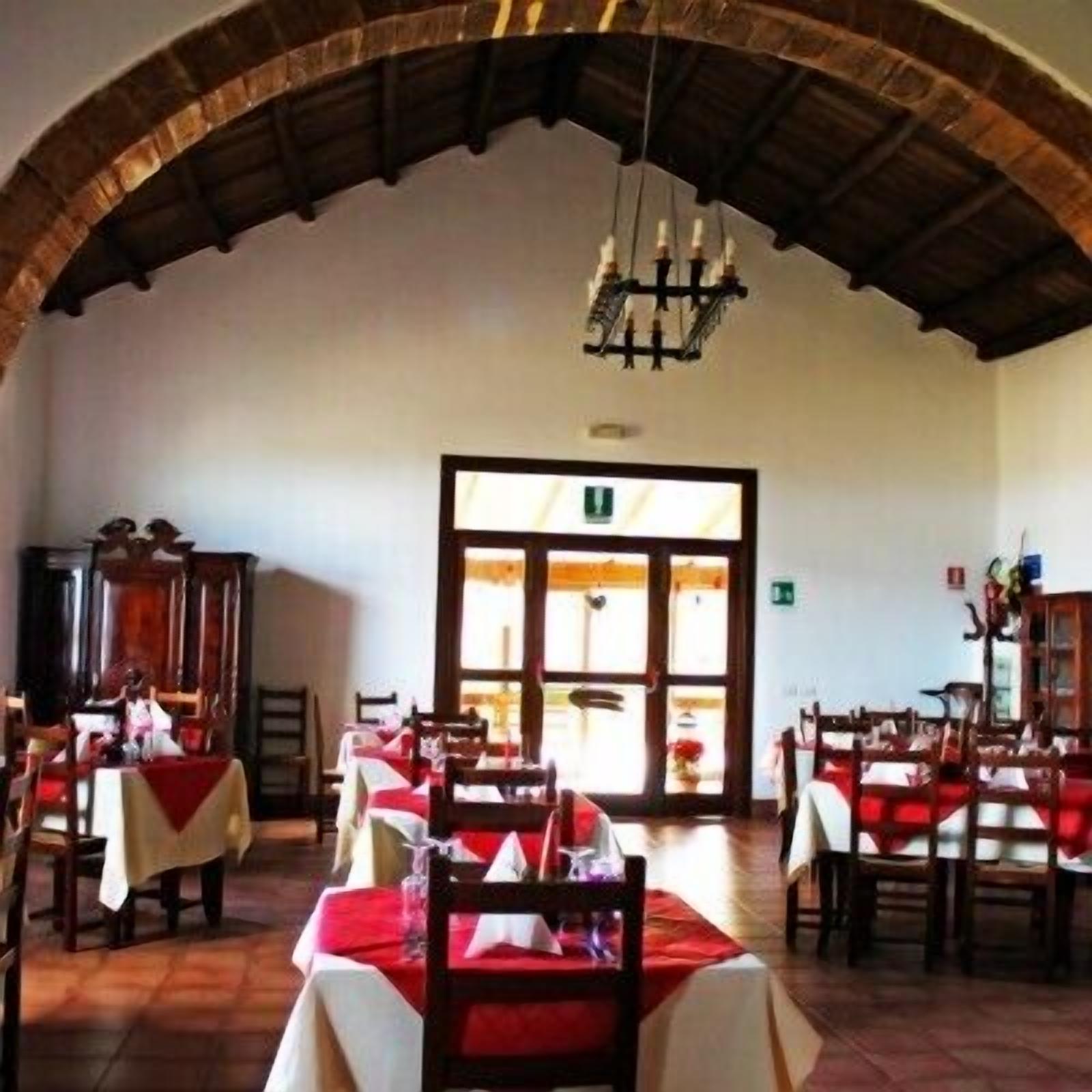 Un comedor con mesas dispuestas para dos, techo de madera y vista a través de un vano.
