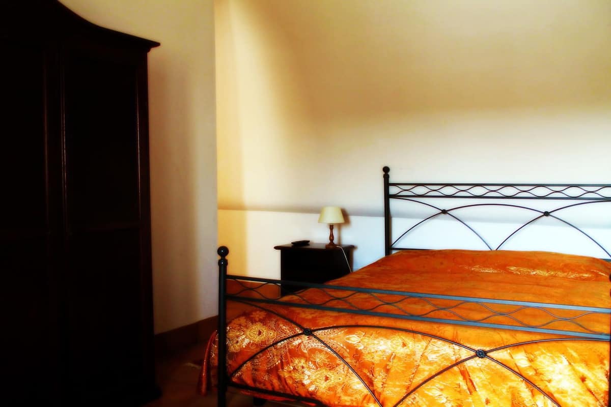 Un letto con copriletto arancione, un comodino con lampada e un armadio in legno scuro.