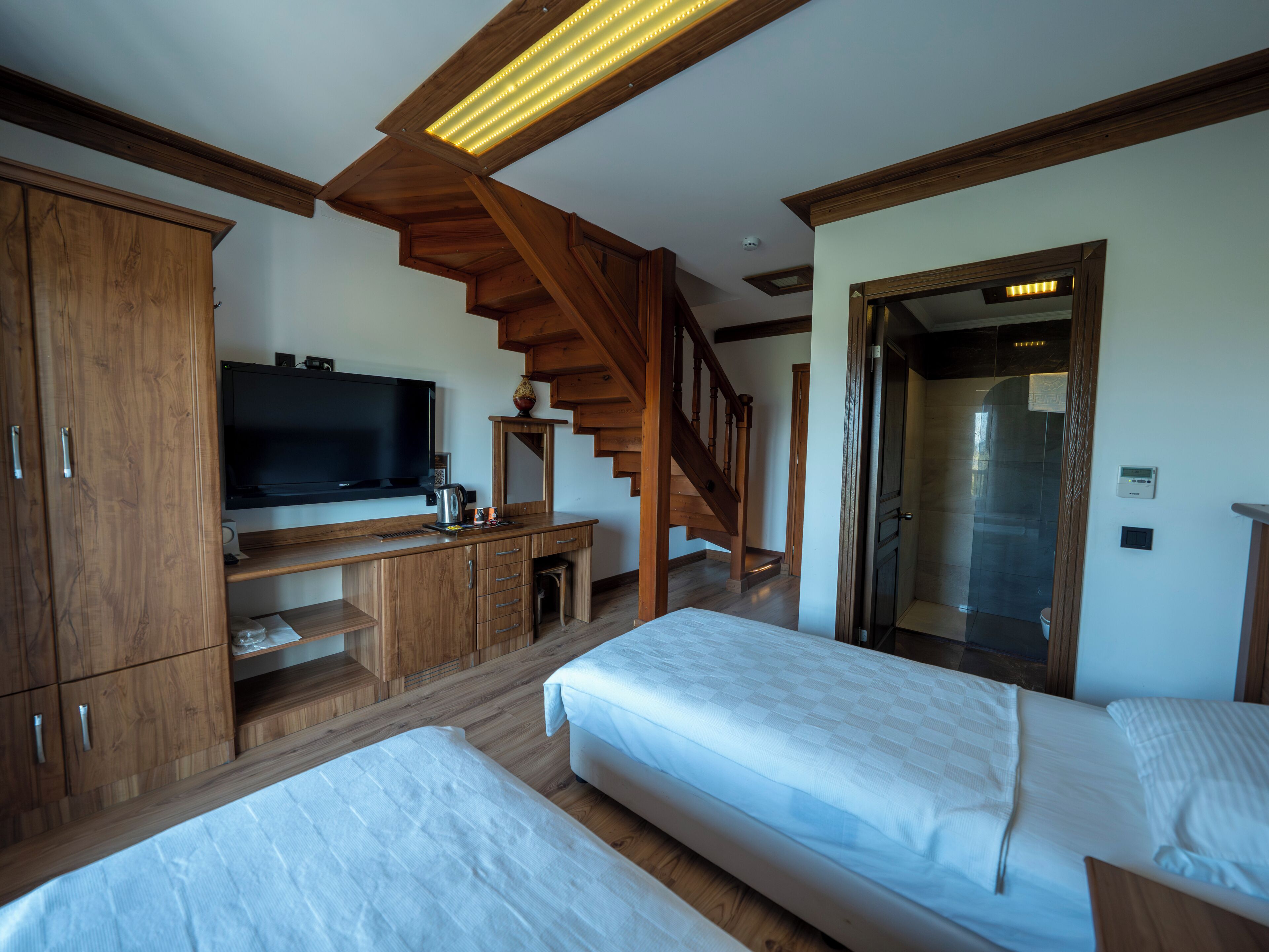Una habitación con dos camas, televisión, muebles de madera, una escalera y una puerta.