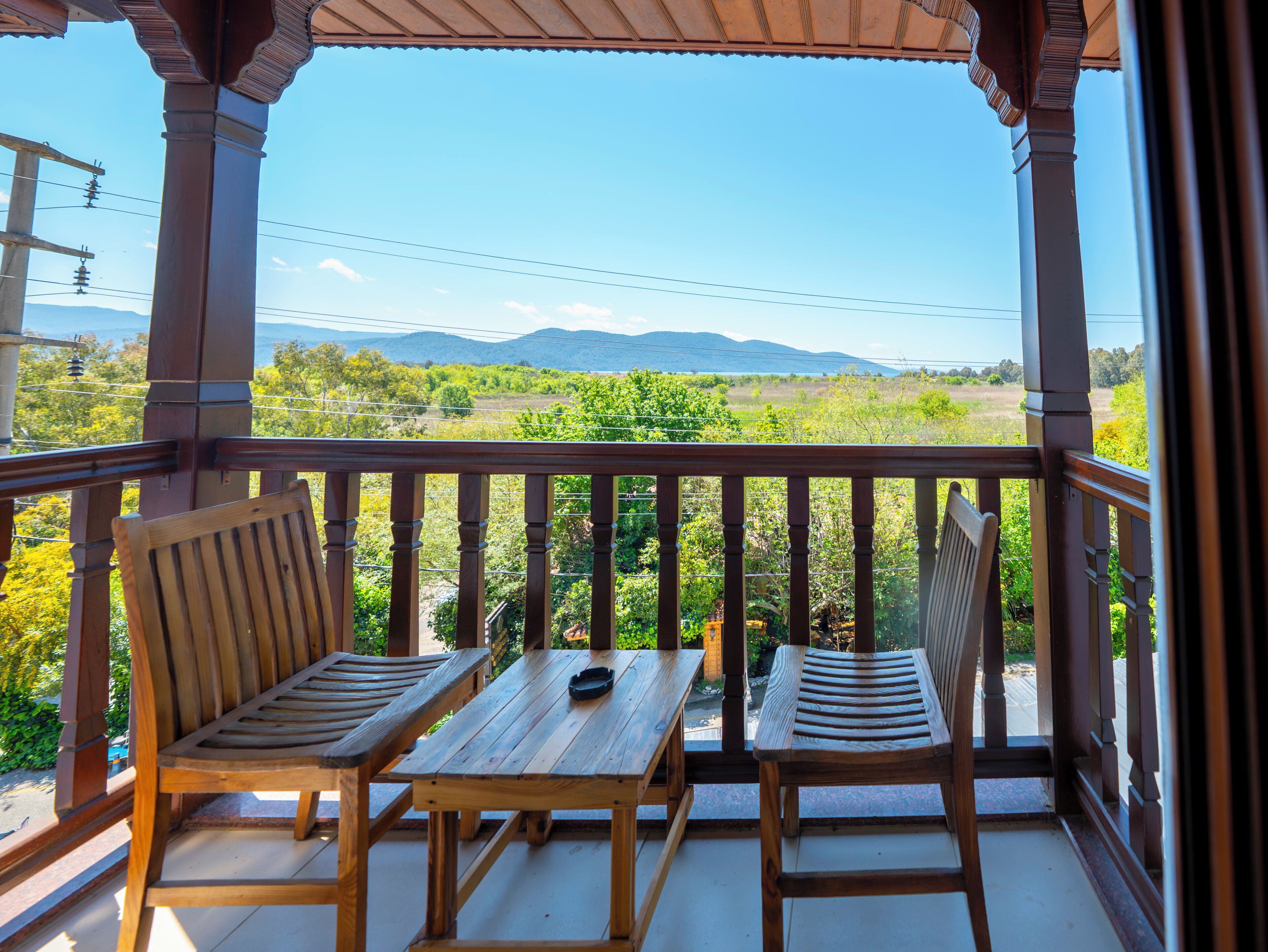 Un balcón de madera con dos sillas y una mesa, con vistas a un paisaje verde y montañas al fondo.