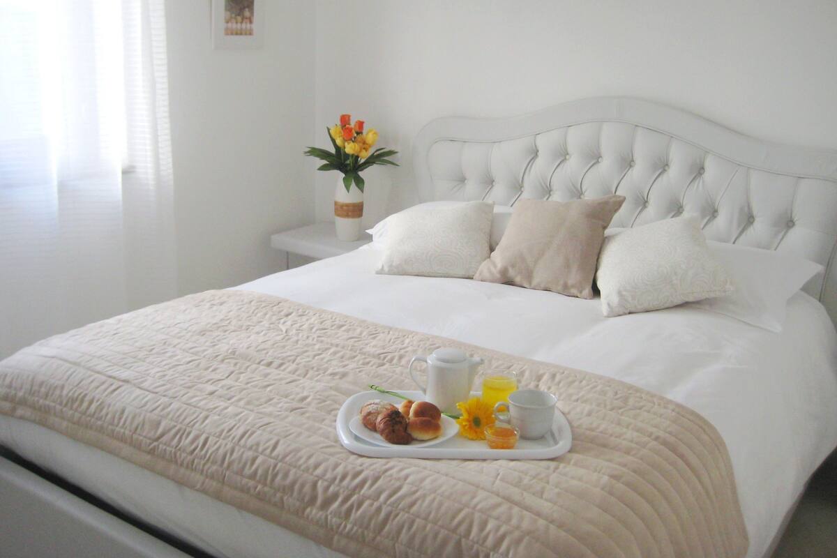 A neatly made bed with a tray of breakfast items, including croissants, a cup, and a glass of orange juice.