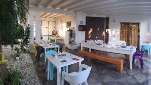 A modern outdoor dining area with white tables and chairs, a wooden bench, and a kitchen area in the background. - B&B Resort Torrefano (Pachino)