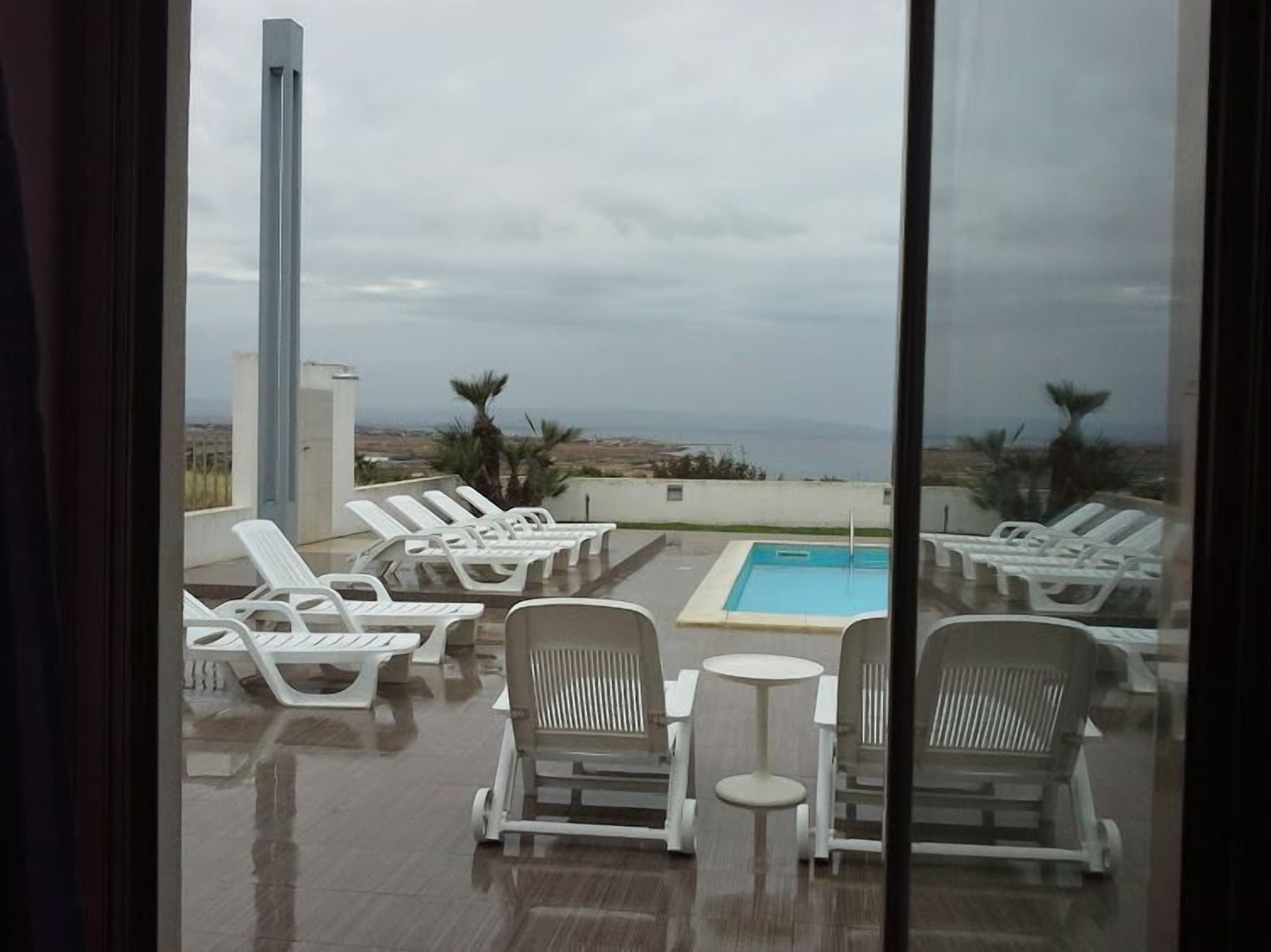 Zona de piscina al terrat amb gandules i una taula petita, amb vista a un paisatge costaner.