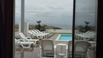 Un espace piscine aménagé sur le toit, avec des chaises longues et une petite table, offrant une vue sur le paysage côtier.